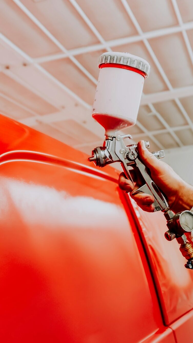 Auto painter spraying red paint on car in auto workshop